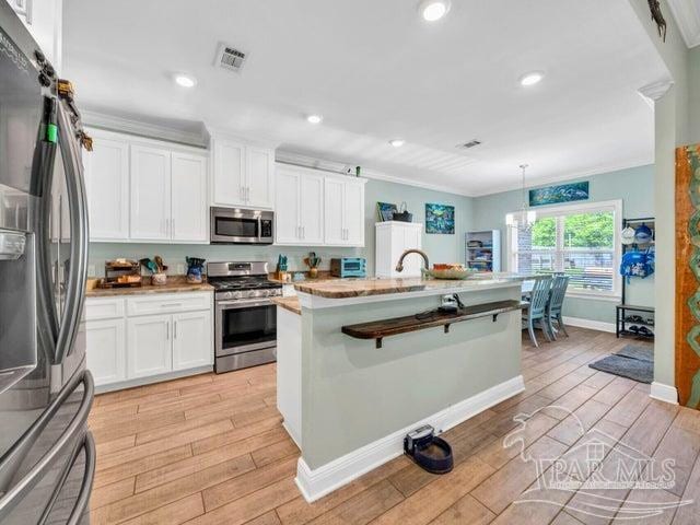1516 Cadence Loop, Cantonment, FL 32533 - kitchen with stainless steel appliances, light wood finished floors, white cabinets, baseboards, and crown molding