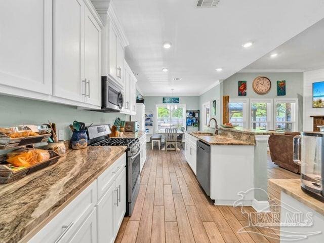 1516 Cadence Loop, Cantonment, FL 32533 - kitchen with appliances with stainless steel finishes, a sink, white cabinets, light wood-style floors, and ornamental molding