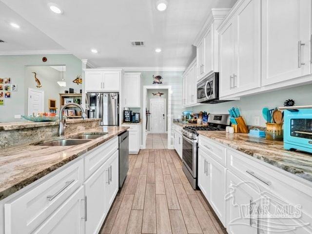 1516 Cadence Loop, Cantonment, FL 32533 - kitchen with stainless steel appliances, a sink, white cabinetry, light wood-style floors, and light stone counters