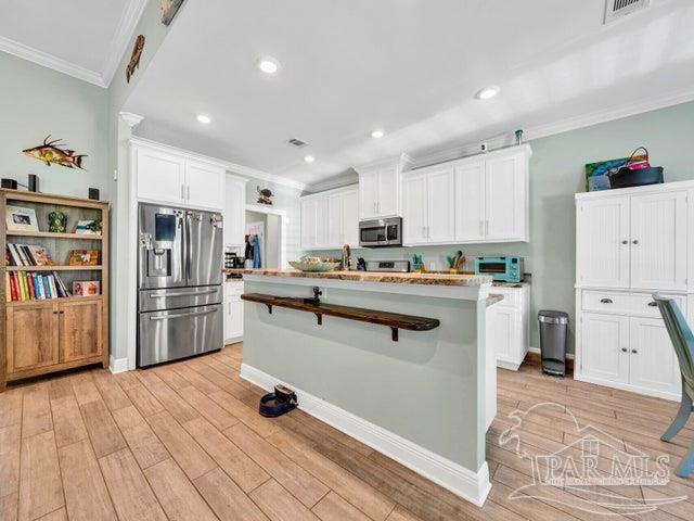 1516 Cadence Loop, Cantonment, FL 32533 - kitchen featuring stainless steel appliances, crown molding, light wood-style floors, white cabinetry, and a kitchen island with sink