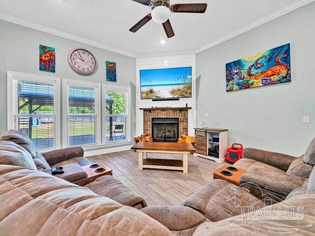 1516 Cadence Loop, Cantonment, FL 32533 - living room featuring ornamental molding, a ceiling fan, wood finished floors, a brick fireplace, and healthy amount of natural light