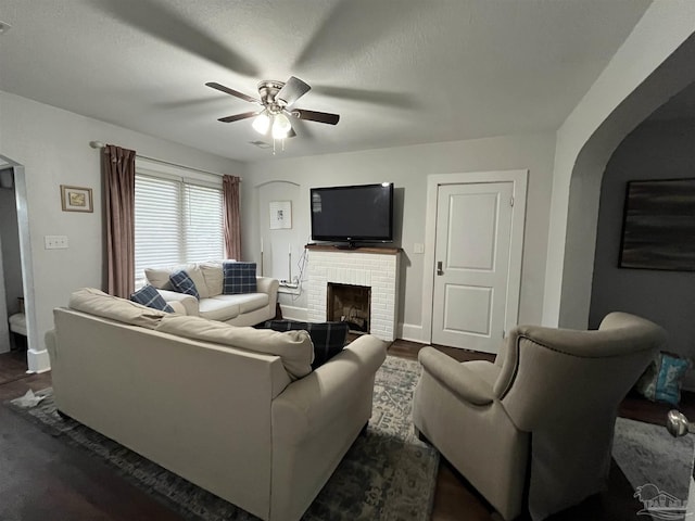 living room with a textured ceiling, ceiling fan, dark hardwood / wood-style flooring, and a fireplace