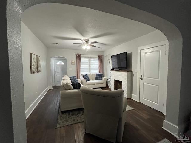 living room featuring ceiling fan, dark hardwood / wood-style floors, and a brick fireplace