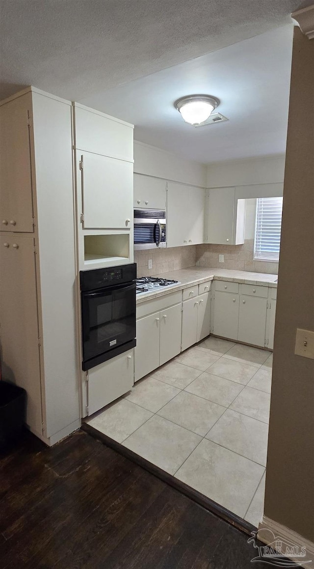 381 Euclid St, Pensacola, FL 32503 - kitchen featuring oven, stainless steel microwave, light countertops, light wood-type flooring, and decorative backsplash