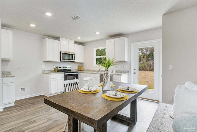 kitchen featuring appliances with stainless steel finishes, a healthy amount of sunlight, white cabinets, and light hardwood / wood-style flooring