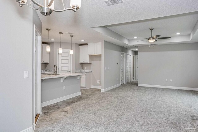 unfurnished living room featuring ceiling fan with notable chandelier, sink, a tray ceiling, light carpet, and a textured ceiling