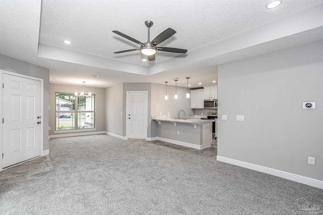 unfurnished living room featuring sink, a textured ceiling, a tray ceiling, ceiling fan with notable chandelier, and carpet