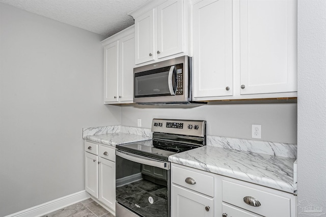 kitchen with white cabinetry, light stone counters, a textured ceiling, and appliances with stainless steel finishes