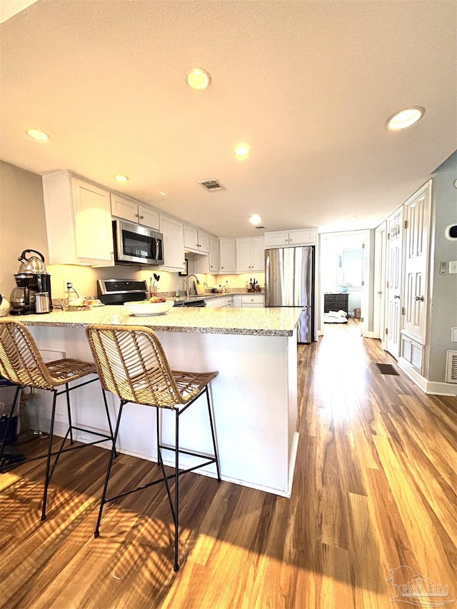 kitchen featuring light stone counters, stainless steel appliances, a peninsula, wood finished floors, and visible vents