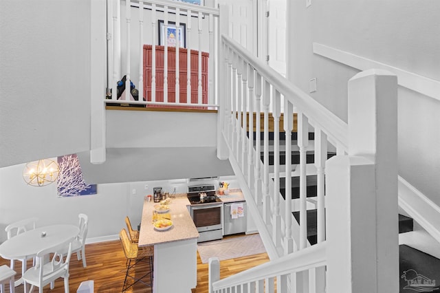 staircase featuring baseboards, an inviting chandelier, wood finished floors, and a towering ceiling