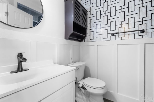 bathroom with vanity, toilet, wainscoting, and a decorative wall