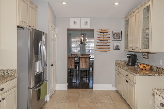 kitchen with a notable chandelier, stone counters, hanging light fixtures, stainless steel fridge with ice dispenser, and cream cabinets