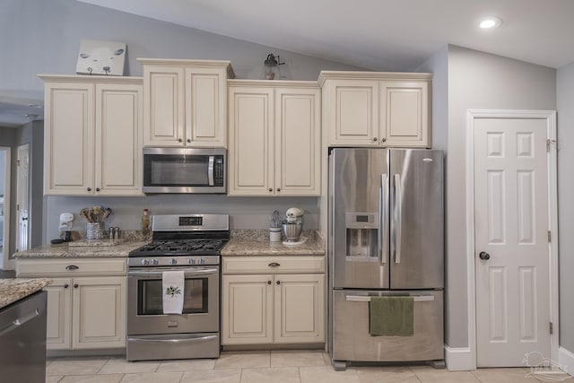 kitchen featuring light tile patterned floors, cream cabinetry, stainless steel appliances, lofted ceiling, and light stone counters