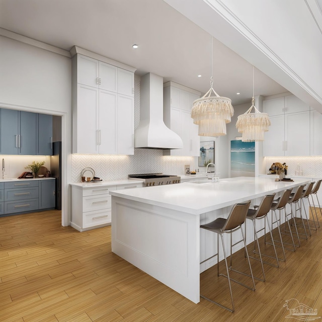 kitchen with an inviting chandelier, wall chimney exhaust hood, a kitchen breakfast bar, light countertops, and backsplash