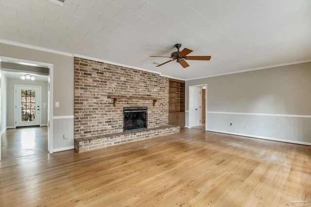 unfurnished living room with ceiling fan, a wainscoted wall, a brick fireplace, wood-type flooring, and crown molding