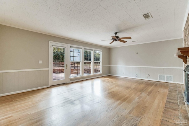 empty room with a brick fireplace, wainscoting, visible vents, and wood finished floors