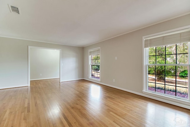 empty room with light wood-style floors, baseboards, visible vents, and ornamental molding