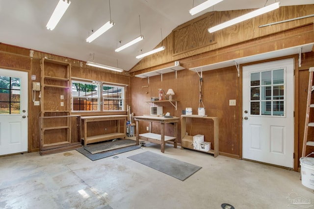 misc room with lofted ceiling, wood walls, and unfinished concrete flooring