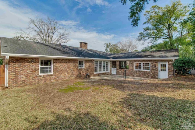 back of house with brick siding, a patio, a chimney, and a lawn