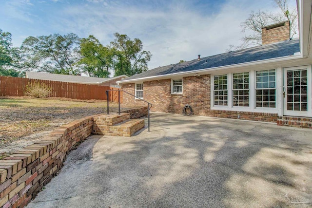 rear view of house with a patio area, brick siding, a chimney, and fence