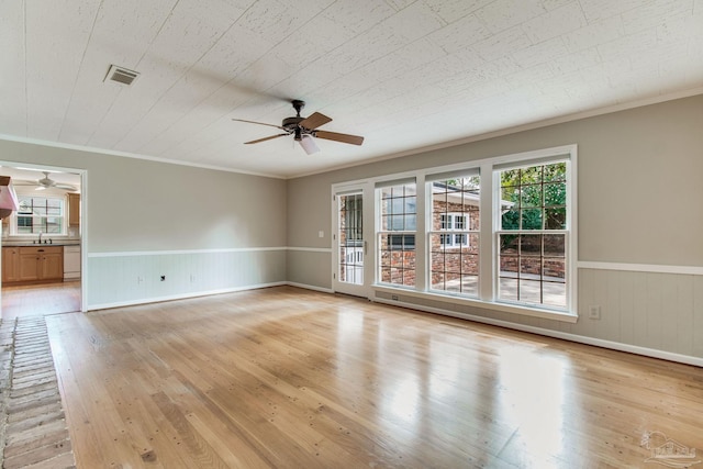 empty room featuring a wainscoted wall, light wood-type flooring, plenty of natural light, and visible vents