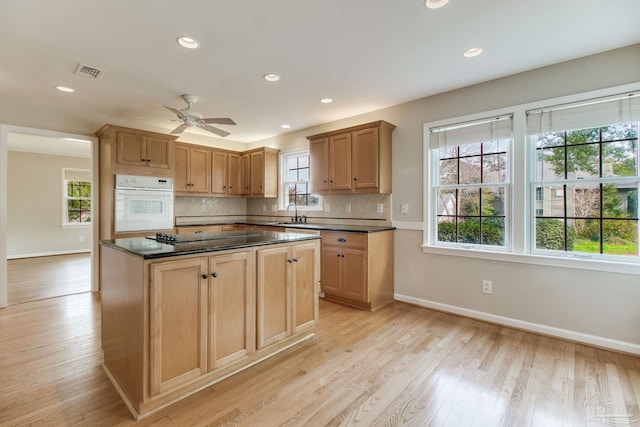 kitchen with black electric stovetop, visible vents, backsplash, light wood-type flooring, and oven