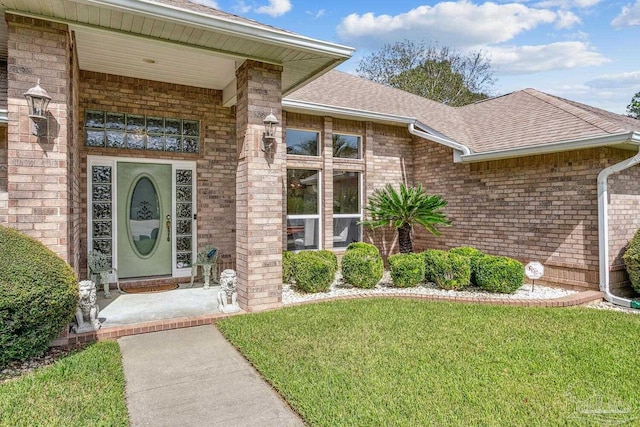 doorway to property featuring a yard, brick siding, and a shingled roof