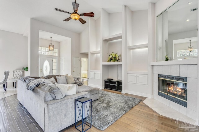 living area with visible vents, built in features, a tile fireplace, wood finished floors, and high vaulted ceiling