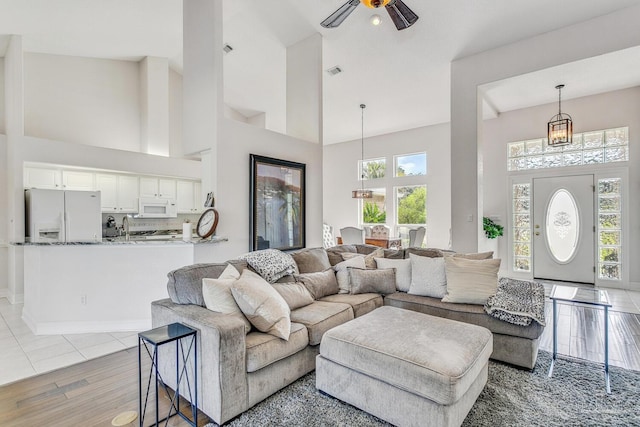 living room with light wood-style floors, visible vents, high vaulted ceiling, and ceiling fan with notable chandelier