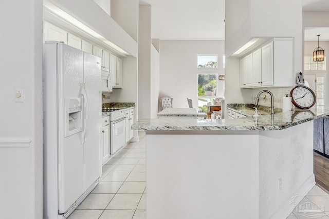 kitchen with light tile patterned flooring, white appliances, a peninsula, and light stone countertops