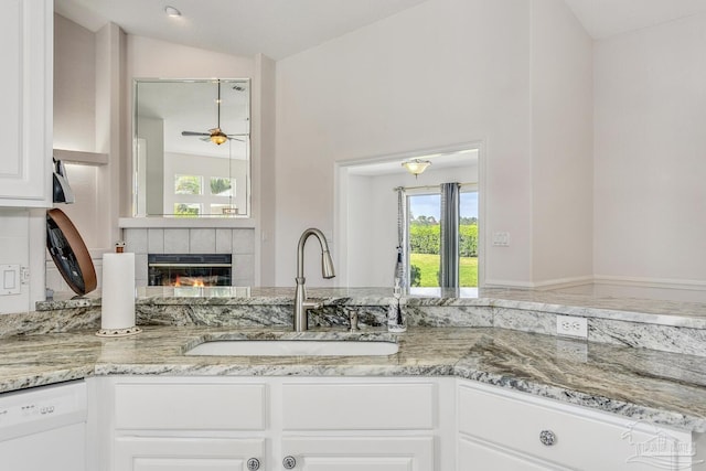 kitchen with a sink, a fireplace, white dishwasher, lofted ceiling, and light stone countertops