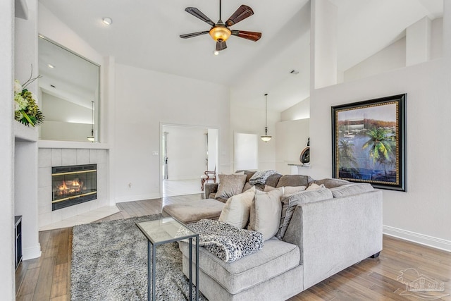 living area with ceiling fan, a tile fireplace, baseboards, and wood finished floors