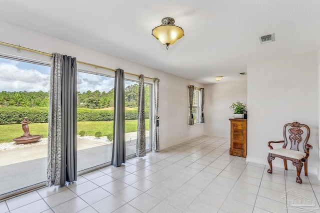 interior space featuring light tile patterned floors, baseboards, visible vents, and a textured ceiling