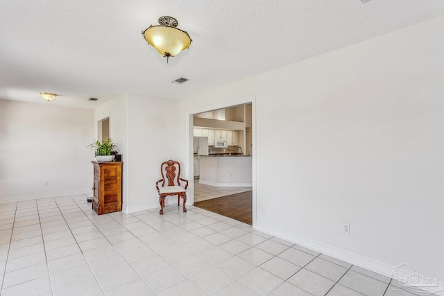 unfurnished room featuring light tile patterned flooring, baseboards, visible vents, and a textured ceiling