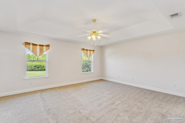 carpeted empty room with a tray ceiling, visible vents, and baseboards