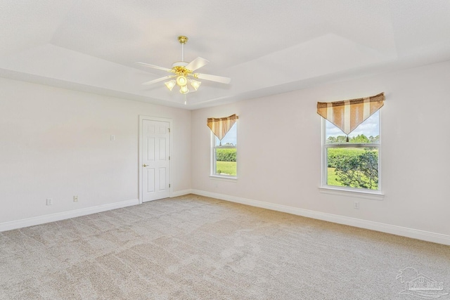 unfurnished room featuring a tray ceiling, baseboards, light colored carpet, and ceiling fan