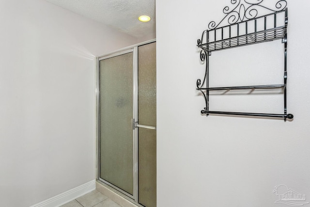 full bath with tile patterned floors, an enclosed shower, a textured ceiling, and baseboards