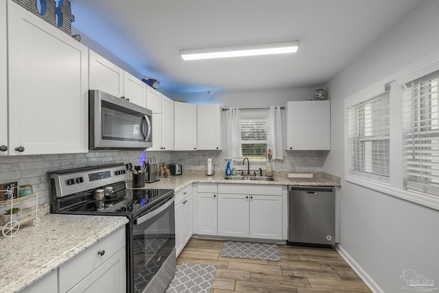 kitchen with a sink, wood finished floors, white cabinetry, stainless steel appliances, and decorative backsplash