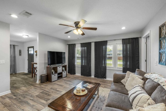 living room featuring visible vents, baseboards, wood finished floors, and a ceiling fan