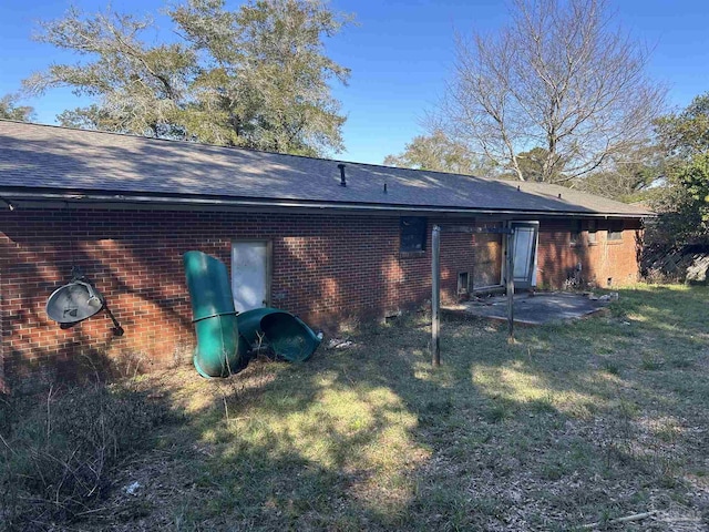 rear view of house with a yard, brick siding, and roof with shingles