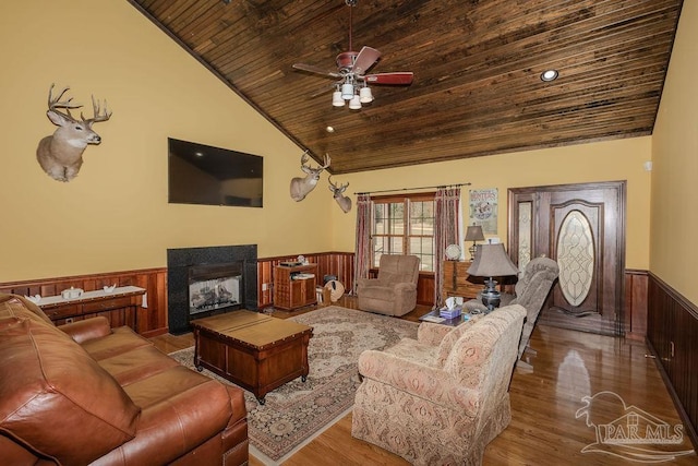 living area featuring a wainscoted wall, ceiling fan, wood finished floors, wooden ceiling, and a multi sided fireplace