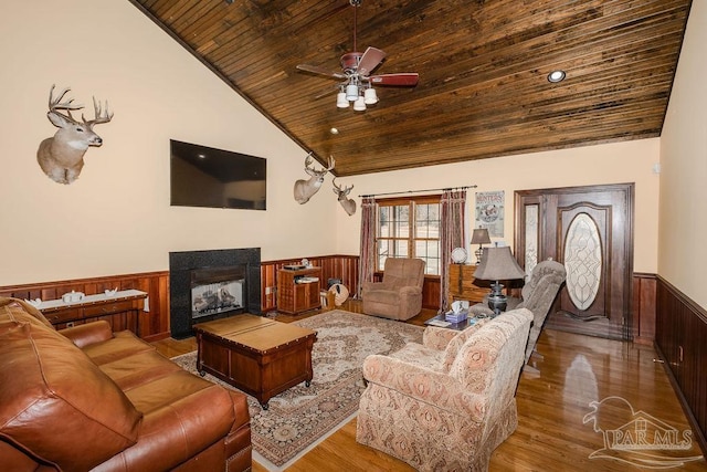 living room featuring a wainscoted wall, lofted ceiling, wood ceiling, wood finished floors, and a multi sided fireplace