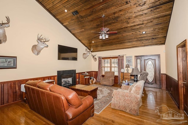 living room with wood finished floors, wainscoting, a multi sided fireplace, and wooden ceiling