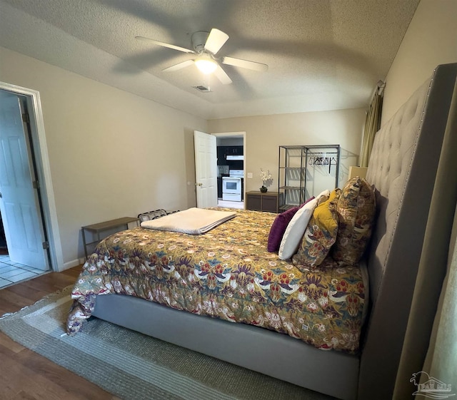 bedroom with a textured ceiling, a ceiling fan, wood finished floors, and visible vents