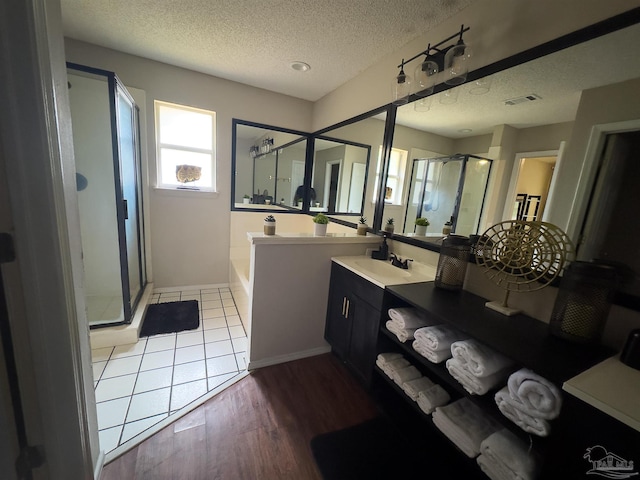full bath featuring vanity, a textured ceiling, wood finished floors, a garden tub, and a stall shower