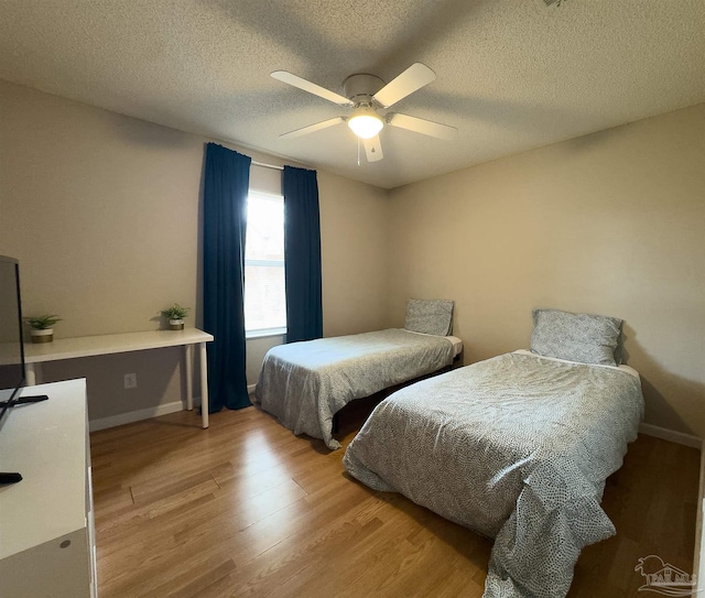 bedroom with baseboards, a ceiling fan, light wood finished floors, and a textured ceiling
