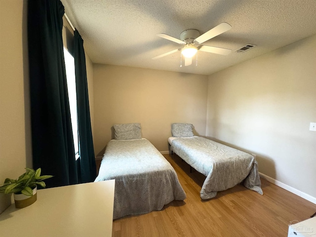 bedroom with visible vents, a textured ceiling, baseboards, and wood finished floors