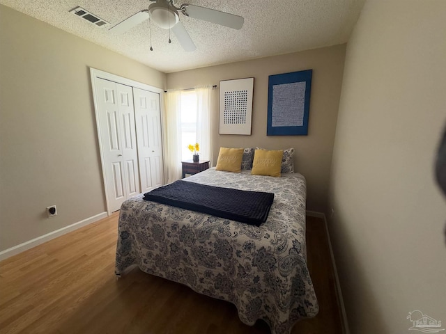 bedroom with a textured ceiling, visible vents, wood finished floors, baseboards, and a closet