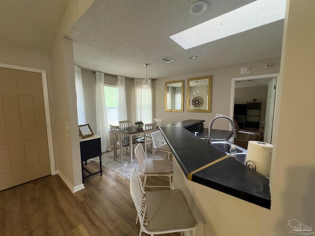 kitchen featuring dark wood-style flooring, a textured ceiling, visible vents, a skylight, and a sink