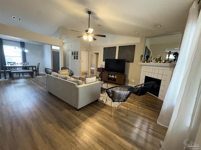 living room featuring a tiled fireplace, ceiling fan with notable chandelier, wood finished floors, vaulted ceiling, and visible vents